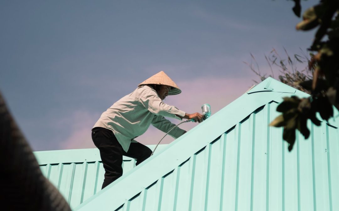 Man in conical hat paints a rooftop, engaging in outdoor work. Low angle view.