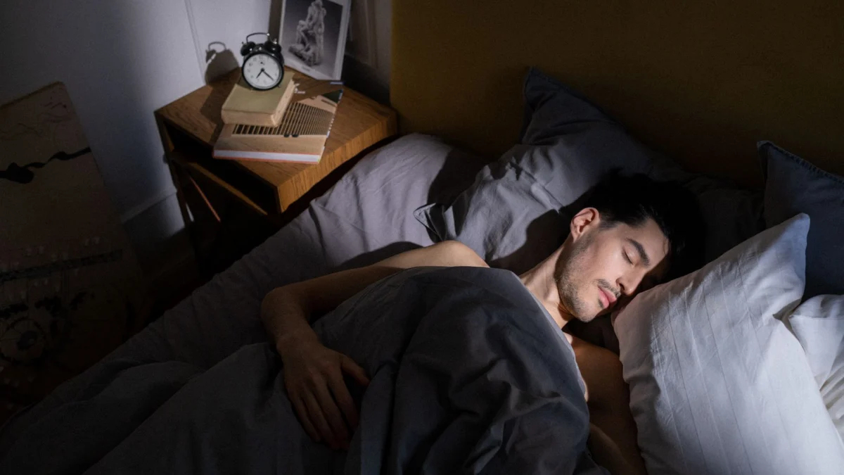 Een man slaapt vredig in bed terwijl het ochtendzonlicht naar binnen stroomt en een serene binnenomgeving creëert.